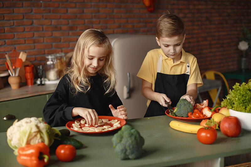 Dwójka dzieci, brat i siostra, przygotowują w kuchni zdrowe posiłki z warzyw i owoców, idealne na budowanie odporności.