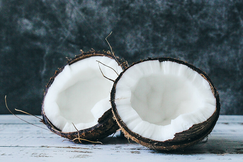 Na drewnianej ławie leży przepołowiony na pół kokos z mięsistym, białym miąższem.
