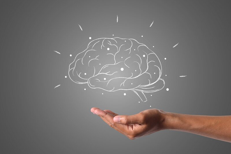 Szkic nad dłonią przedstawia mózg podczas pracy, otoczony opieką człowieka. 